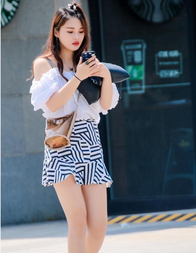 街拍:美女身穿白色的短款t恤,搭配一个黑色的长筒靴,秀丽迷人