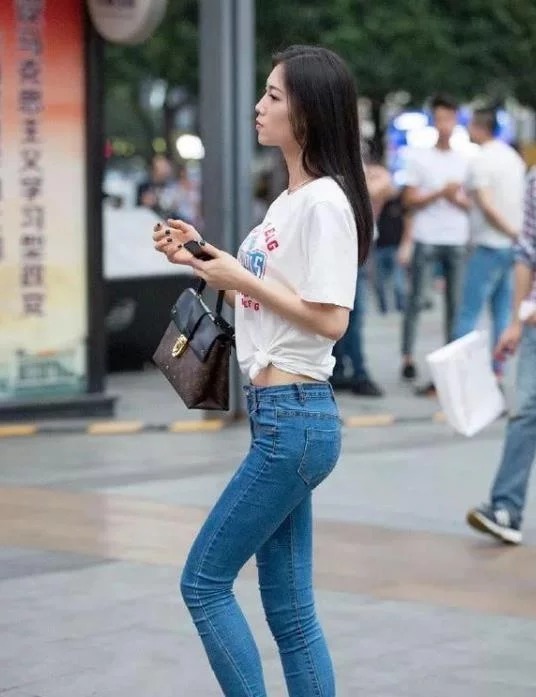 牛仔裤|街拍:肤如凝脂的美女,身穿白色背心配浅色牛仔裤,青春靓丽气质