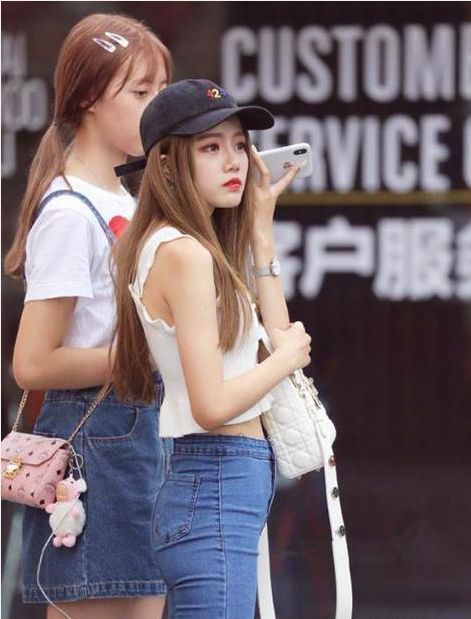 穿着白色|街拍：小姐姐穿着白色的吊带背心搭配牛仔长裤，气质甜美性感