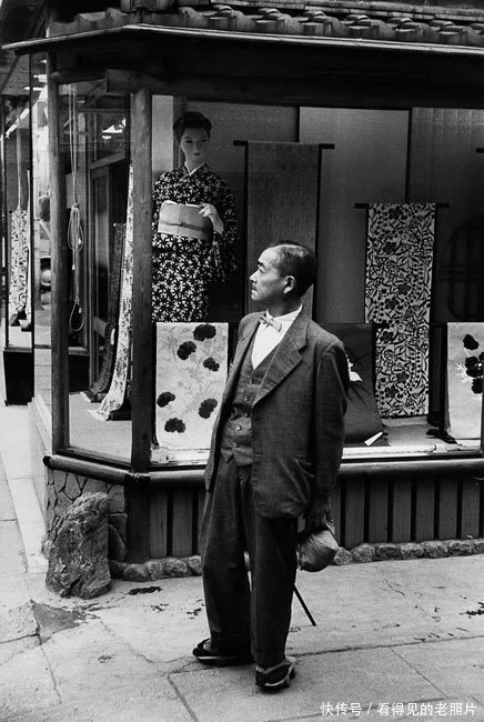 身穿西装的日本男子，身后是传统的和服裁缝店。