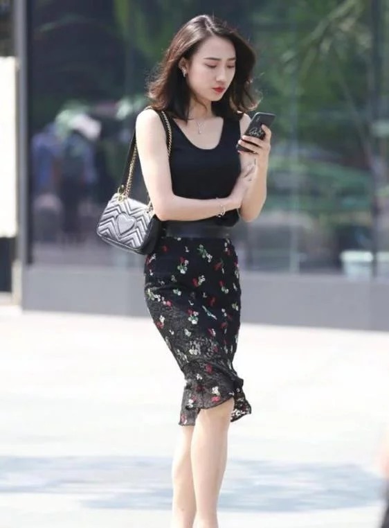 背心|街拍:专注手机的美女,背心配黑色碎花裙,凸显完美身材